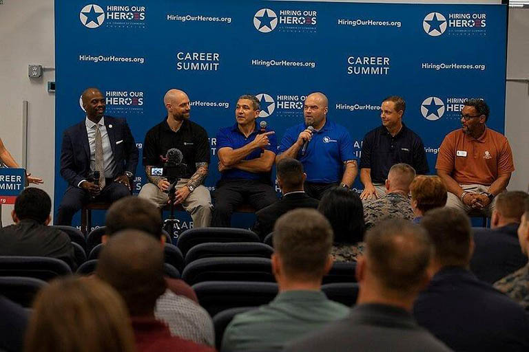 Six males sit in a row on a speakers panel